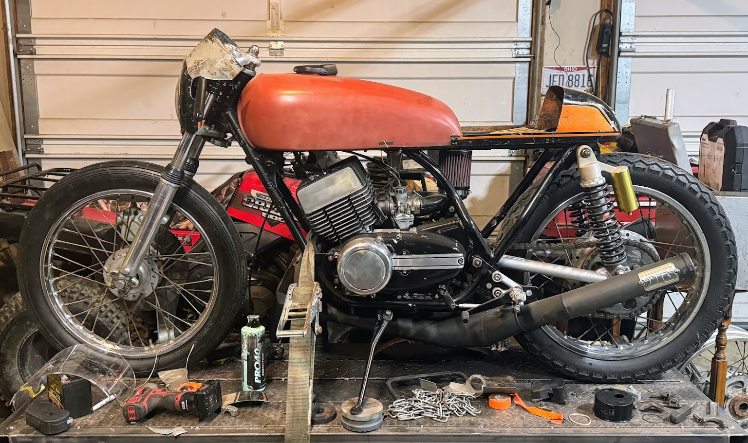 A Yamaha RD350 cafe racer mid-build, strapped to a bench with tools laid out